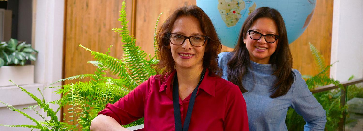 Jennifer Reyes and Claudia Chambers smiling next to each other by an inflatable globe and ferns