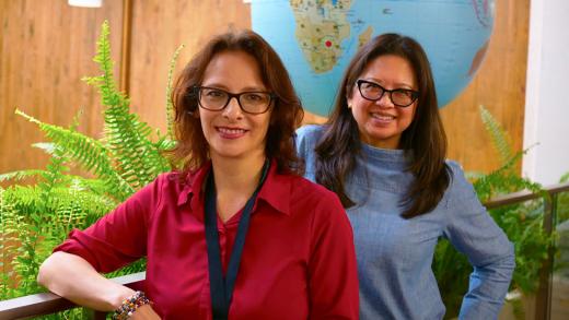 Claudia Chambers and Jennifer Reyes smile together next to ferns and an inflatable globe.