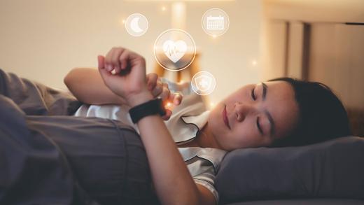 Woman lying in bed looking at her watch, which displays moon, heartbeat, calendar, and medical icons