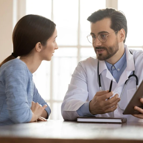 A doctor sits at a table speaking with a patient.