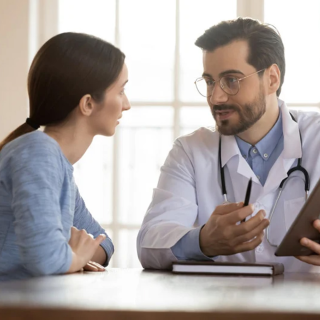 A doctor sits at a table speaking with a patient. 