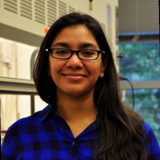 Anam smiles in a blue shirt and black glasses