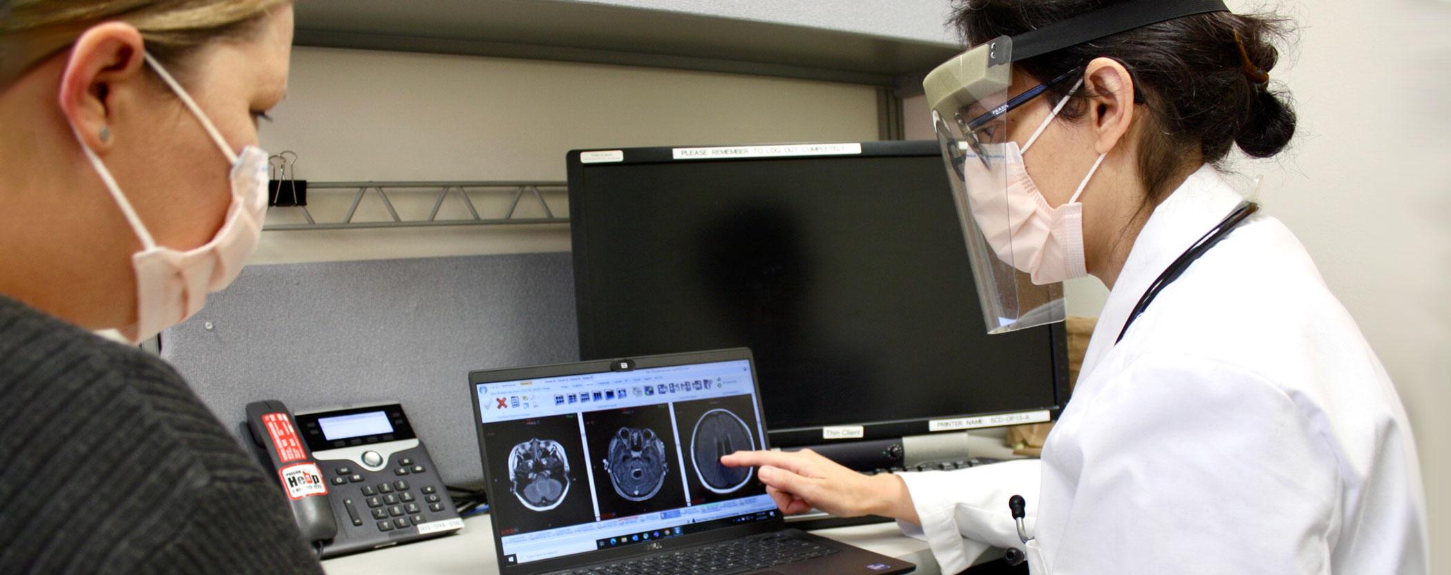 Doctor and patient with face masks sitting at computer looking at MRI brain images
