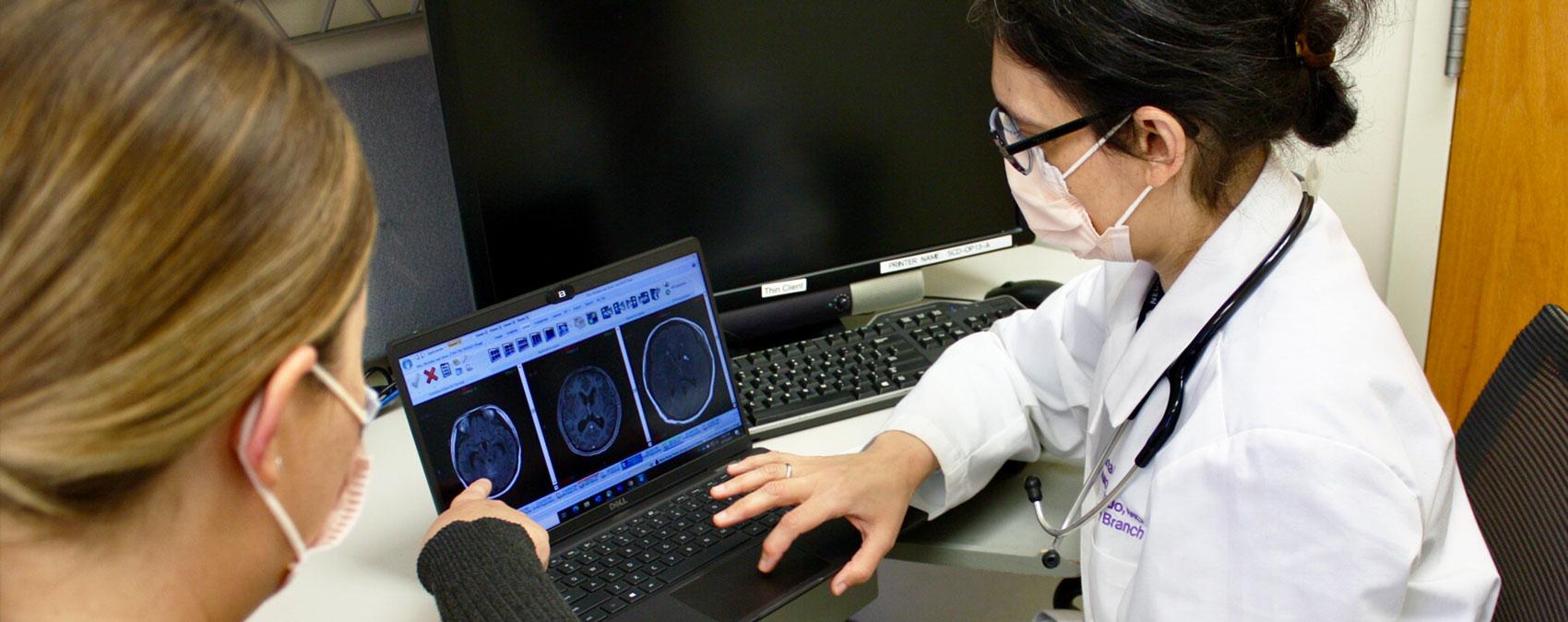 Doctor and patient wearing face masks and seated at a computer looking at brain MRI scans