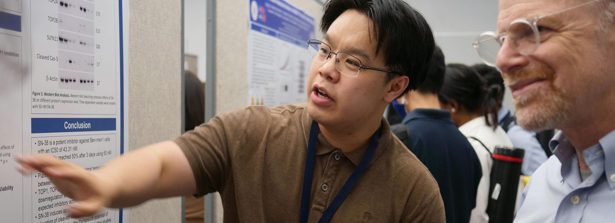 Postbac fellow explaining his scientific poster to an attendee at a conference.