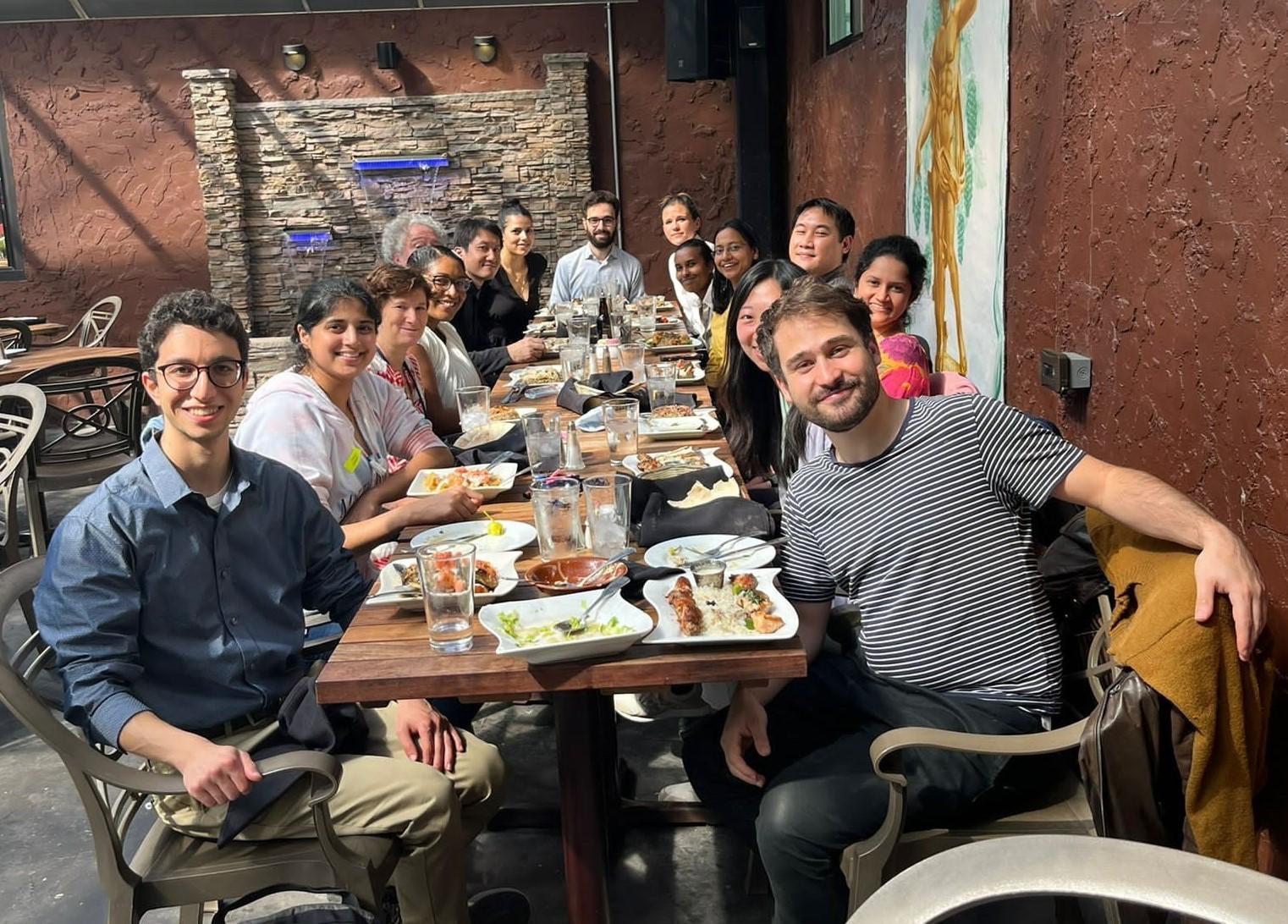 Members of the Taylor lab are gathered at a long table, smiling and looking at the camera.