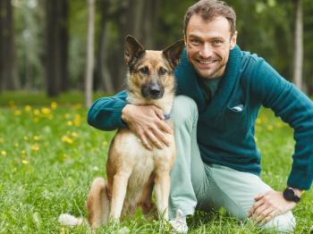 A man smiling and kneeling down with his arm around his dog.